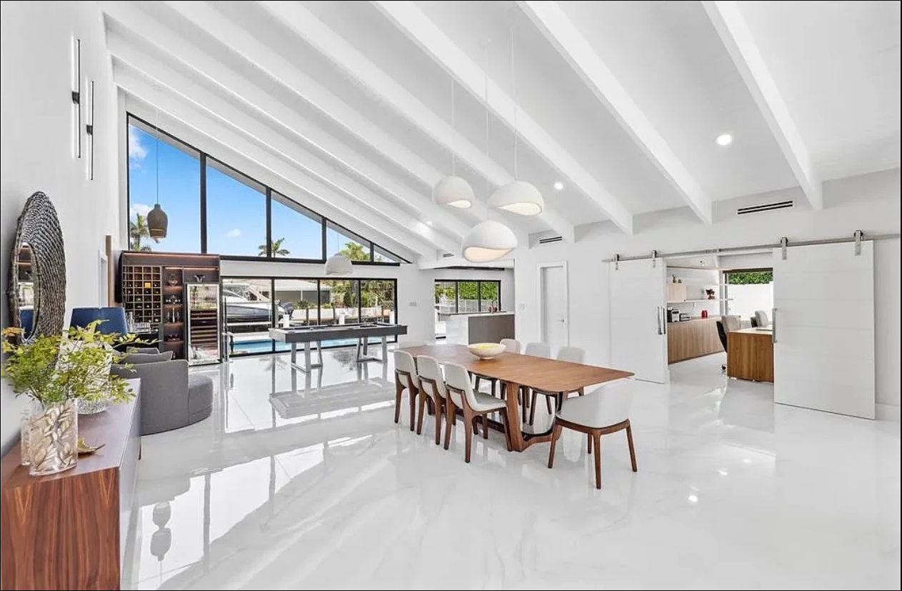 Wood dining table under a beamed ceiling beside an open kitchen