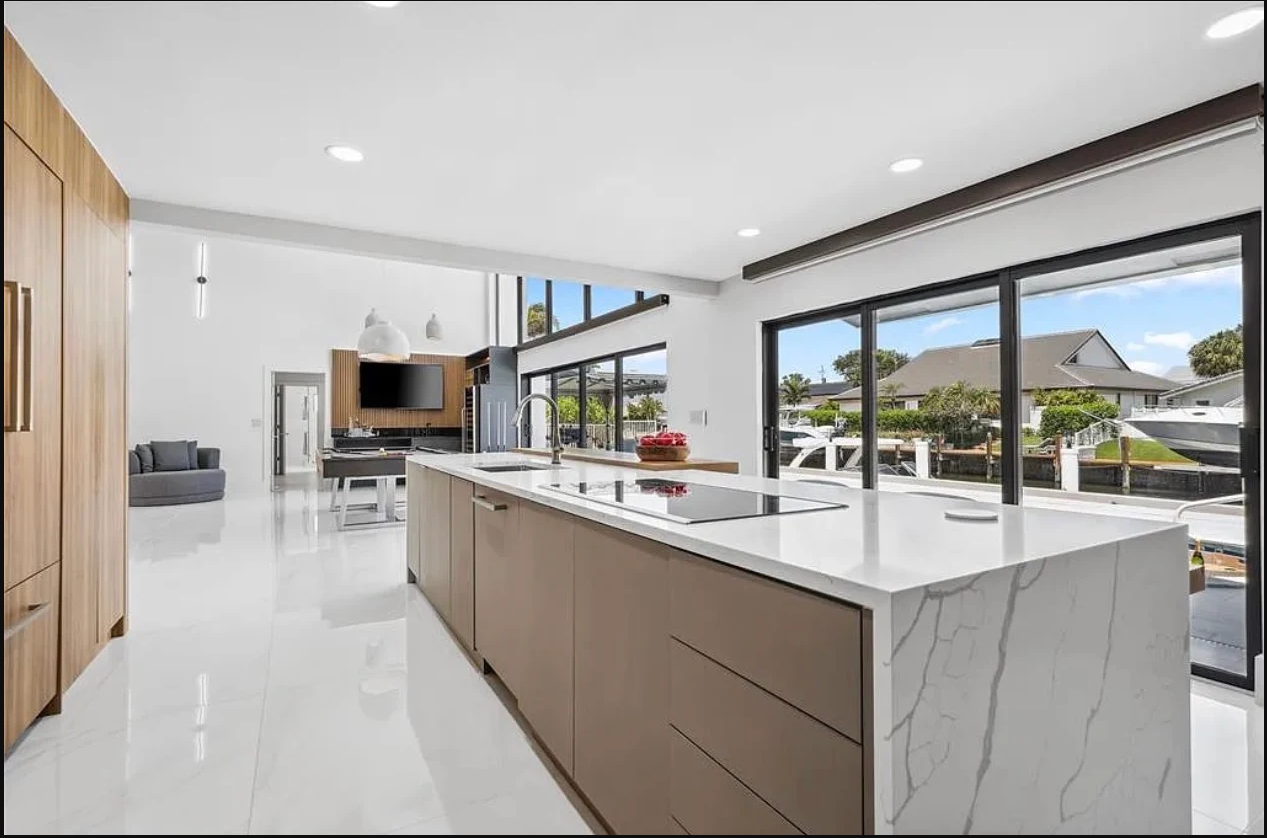 Completed coastal kitchen with wood cabinetry, a long stone island, and wide windows