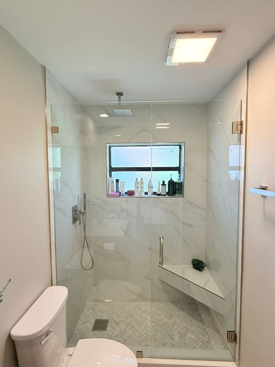 Light shower with a glass enclosure, corner bench, and herringbone-pattern floor