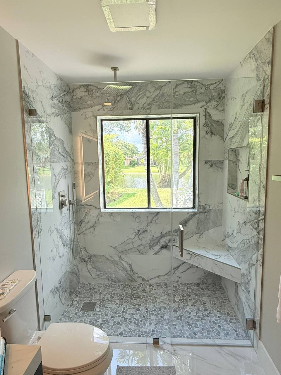 Glass shower with bold veining, a corner bench, and pebble-pattern floor