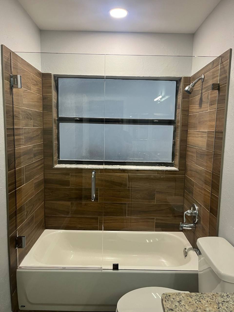 Bathtub and glass enclosure framed by wood-look tile
